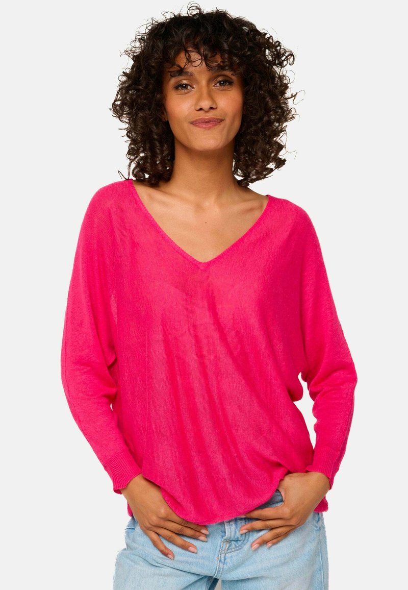 Rosa V-Ausschnitt-Pullover mit langen Ärmeln, lockerer Passform, leichtem Material und Rippdetails an den Bündchen, kombiniert mit hellblauen Jeans.