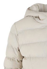 Dunjakke i lys beige. Har quiltet tekstur, høj krave og en glat stoffinish. Ingen synlige beslag eller pynt.