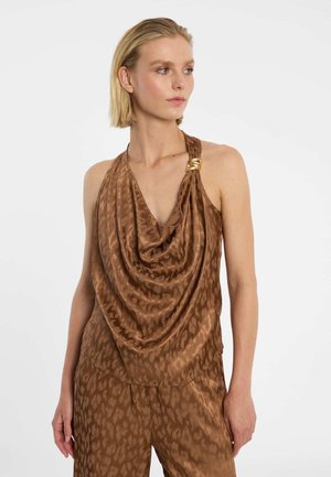 Femme portant un haut en satin marron à col bénitier avec un fermoir doré, associé à un pantalon assorti à motif, regardant de côté.