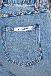Tylna kieszeń jasnoniebieskich dżinsów z białą metką z napisem „#TrueSize” czarnym tekstem.