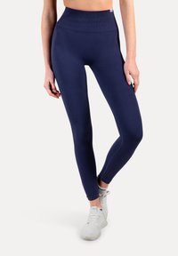 Granatowe legginsy z wysokim stanem o bezszwowej fakturze, dopasowane na całej długości, z elastycznym pasem. Połączone z białymi butami sportowymi.