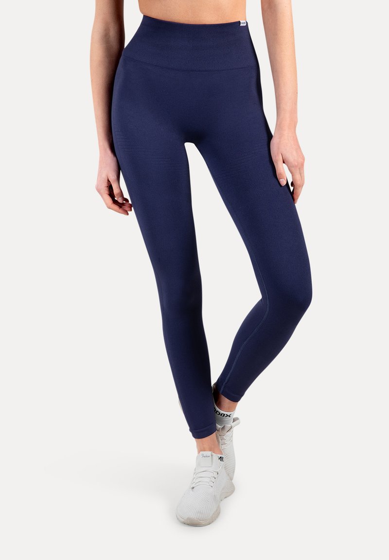 Granatowe legginsy z wysokim stanem o bezszwowej fakturze, dopasowane na całej długości, z elastycznym pasem. Połączone z białymi butami sportowymi.