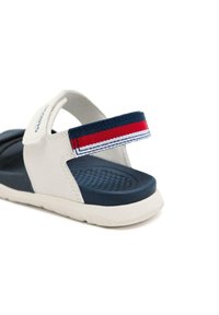 Sandalia de playa blanca con suela azul marino, plantilla texturizada y tira ajustable de rayas multicolor en rojo, blanco y azul.
