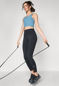 Αθλητική ένδυση με ανοιχτό μπλε κοντό μπλουζάκι και μαύρες ψηλόμεσες κολάν με το λογότυπο Nike. Μαύρα αθλητικά παπούτσια με υφή.