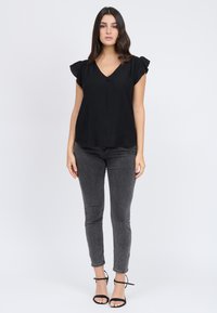 Top nero a maniche corte con design a V; presenta una sottile trama e dettagli arricciati alle maniche. Abbinato a jeans skinny grigi e tacchi neri.