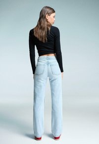 Svijetloplave široke traperice s visokim strukom, vidljivim stražnjim džepovima i izblijedjelom teksturom, uparene s crnim priljubljenim topom s dugim rukavima.