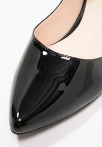 Chaussure plate à bout pointu en cuir verni noir avec doublure intérieure beige sur fond blanc.
