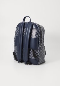 Mochila azul marítimo com um padrão texturizado, apresentando alças acolchoadas e fecho com zip. Fabricada em materiais duráveis, possui bolsos laterais.