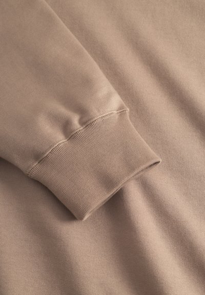 Primo piano del tessuto di un pullover beige, con un polsino a coste che presenta una texture liscia e una finitura morbida, lievemente spazzolata.