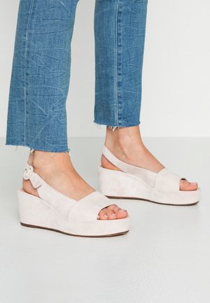 Light beige suede wedge sandals with an open toe design, adjustable ankle strap, and textured surface. Pairing with cropped blue denim.