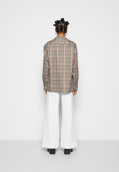 Camisa quadriculada em tons de cinza, vermelho e bege; mangas longas; coleira clássica; combinada com calças largas brancas; detalhes de design minimalistas.
