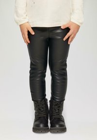 Zwarte synthetische leren leggings gecombineerd met zwarte enkellaarzen met een gestructureerde afwerking en ritssluiting aan de zijkanten.