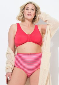 Top bikini rosso senza fili con chiusura frontale, abbinato a slip a vita alta rosa e bianchi a righe. Texture morbida, senza stampe o decorazioni.