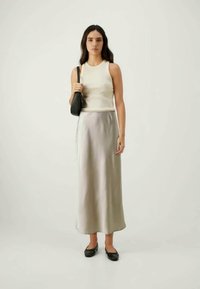 Top branco sem mangas combinado com uma saia longa de seda prateada. Bolsa preta e sapatos planos pretos. Textura suave, design minimalista, aparência elegante.