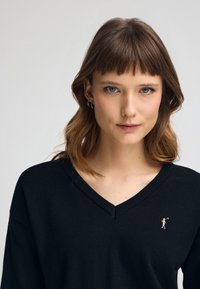 Maglione nero a V realizzato in morbido tessuto a maglia, caratterizzato da un piccolo logo ricamato in rosa sul lato sinistro e una texture liscia.