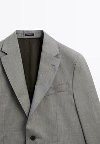 Hellgrauer Blazer mit strukturiertem Revers, einreihiger Knopfleiste und Brusttasche. Glatte Textur mit dezentem, gemustertem Gewebe.