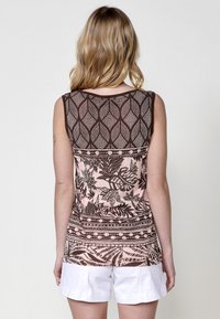 Haut sans manches marron et rose à motifs de feuilles, en matériau doux, avec un col rond, associé à un short blanc.