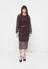 Costum format din două piese, cu paiete, în burgundă închisă, având un top scurt cu mâneci lungi și o fustă până la genunchi cu o siluetă ajustată.