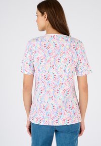 Korte mouwen bloes met een patroon van pasteltinten, versierd met kleine rode en blauwe bloemen op een witte achtergrond.