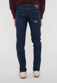 Jeans in denim blu scuro con vestibilità slim, dotati di cuciture arancioni, due tasche posteriori e un'etichetta in pelle marrone con il marchio in vita.