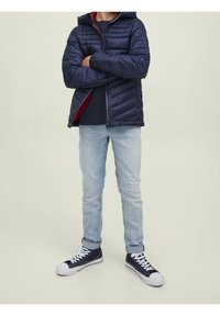 Námořnická puffer bunda s kapucí, prošívaná texturou, červenou podšívkou, spárovaná se světle modrými džíny a námořnickými teniskami s bílými akcenty.