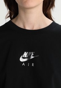Čern é bavlněné tričko s kulatým výstřihem, které v centru zobrazuje stříbrné logo Nike Air. Jednoduchý design s hladkou strukturou.