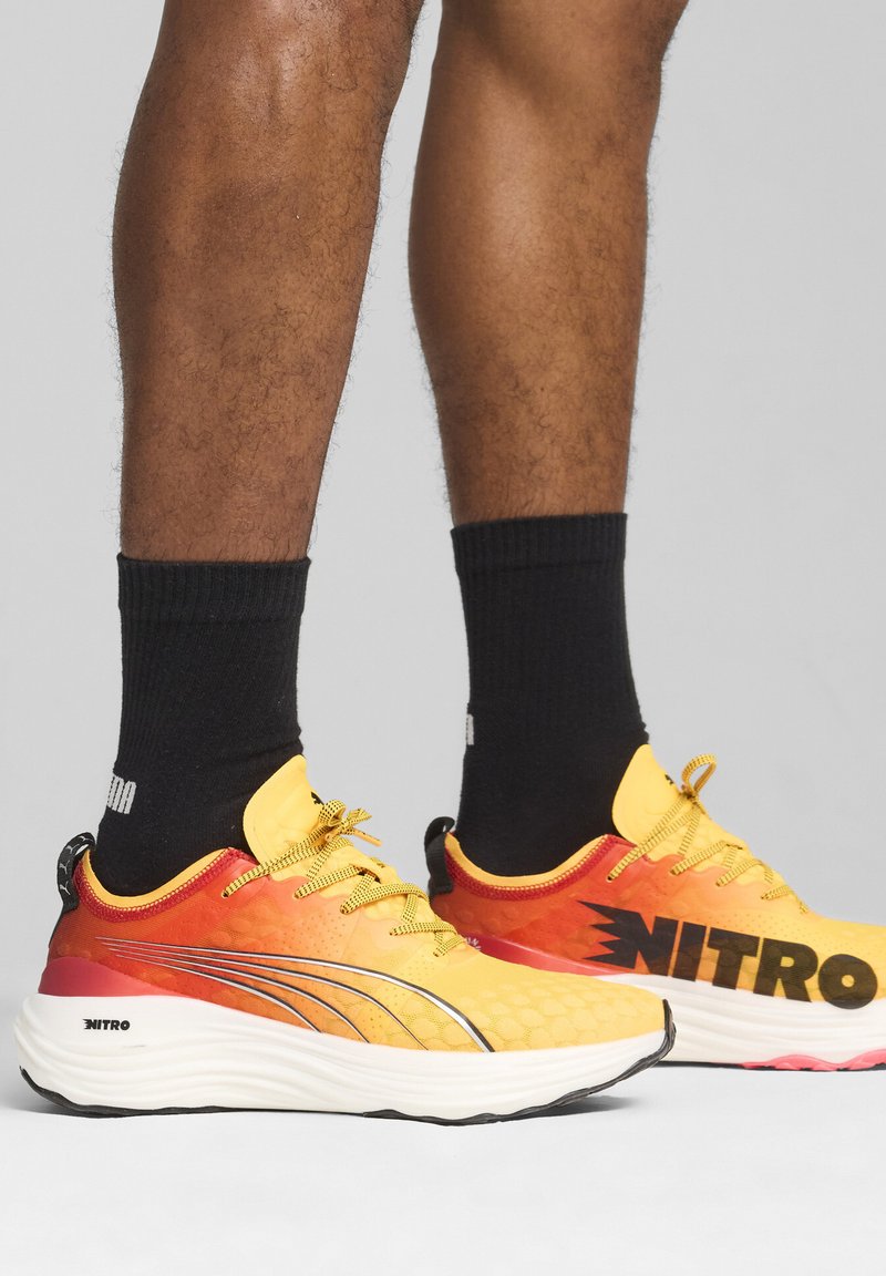 Zapatillas de running amarillas brillantes con acentos rojos, con una textura de panal, marca en negro, detalles reflectantes y una suela acolchada.