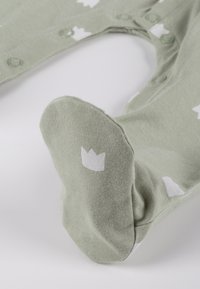 Tutina verde chiaro per neonati realizzata in tessuto morbido. Presenta motivi bianchi di corone e bottoni per la chiusura. Design con piedini morbidi per il comfort.