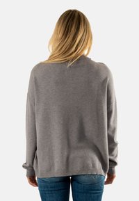 Sudadera gris de gran tamaño con un cuello redondo y puños y dobladillo acanalados. Textura suave, corte casual. Combinada con jeans de color azul claro.
