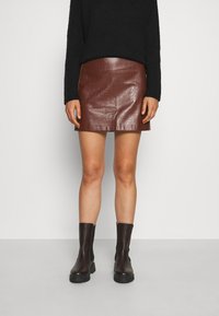 Korta kjol i brun konstläder med krokodilstruktur, i kombination med svarta ankelstövlar och en svart stickad tröja. Enkelt och stilrent design.