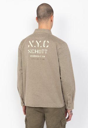 Khaki cotton long-sleeve shirt with button cuffs, featuring a white printed design on the back, including “NYC” and “SCHOTT” text.