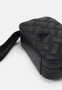 Borsa nera in pelle trapuntata con forma rettangolare, caratterizzata da una finitura testurizzata e un ornato emblema di un uccello nero sul fronte.
