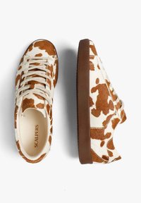Zapatillas con estampado de vaca, confeccionadas en un tejido texturizado en marrón y crema, con punta redonda, diseño con cordones y suela de goma marrón.