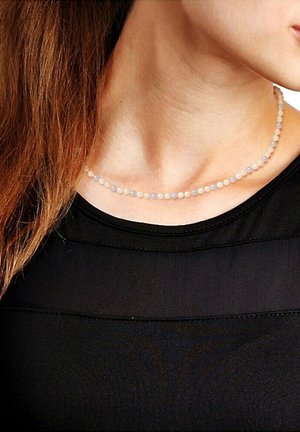 Collier en perles avec de petites perles rondes de couleur violet clair et translucide. Porté autour du cou, contrastant avec un haut noir.