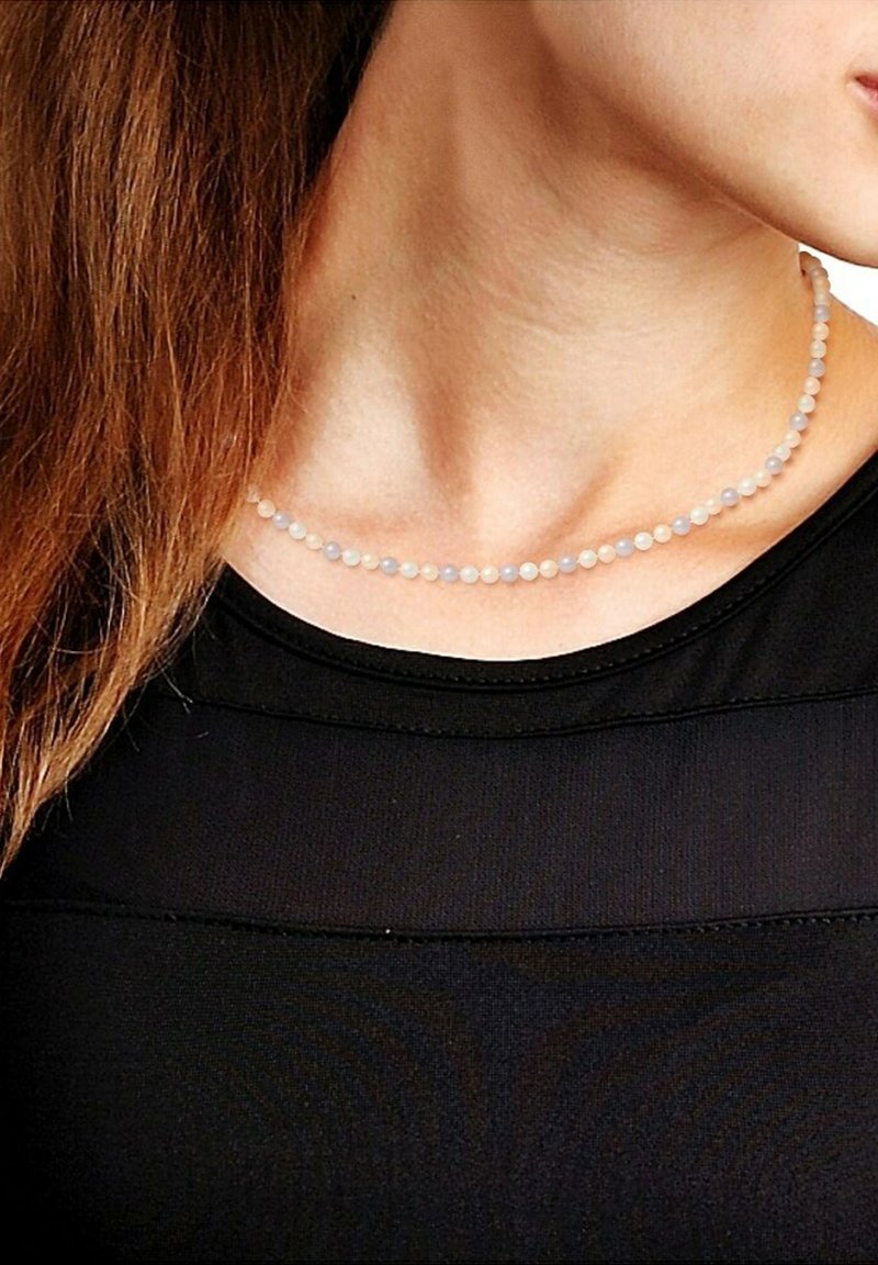 Collier en perles avec de petites perles rondes de couleur violet clair et translucide. Porté autour du cou, contrastant avec un haut noir.
