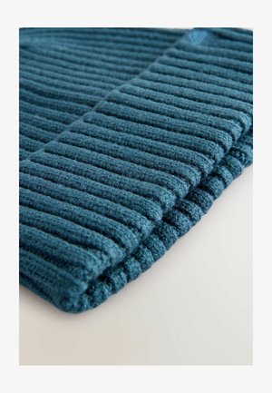 Tessuto a coste color turchese che mette in risalto una consistenza morbida, caratterizzato da file di righe in rilievo e un bordo ripiegato, offrendo un aspetto accogliente.