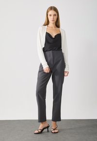 Black cowl neck top, cream cropped cardigan, tailored gray trousers, and black strappy heels. Smooth fabric with defined seams and structured fit.