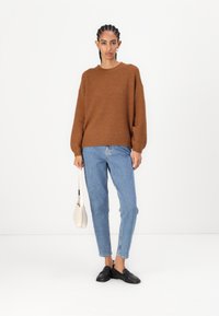 Brown, ribbed knit sweater with dropped shoulders, paired with light blue, straight-leg jeans. Lightweight white handbag and black shoes.