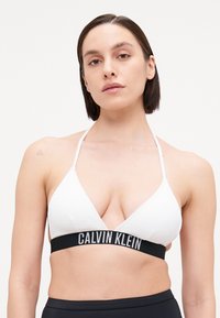 White ribbed triangle bikini top with thin straps, featuring a black elastic band with "CALVIN KLEIN" in white lettering.