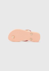 Flip-flop näkymä pohjalta, jossa on teksturoitu vaaleanpunainen pohja, pyöreät puuakkentit ja hienovarainen hohde hihnadesignissä.