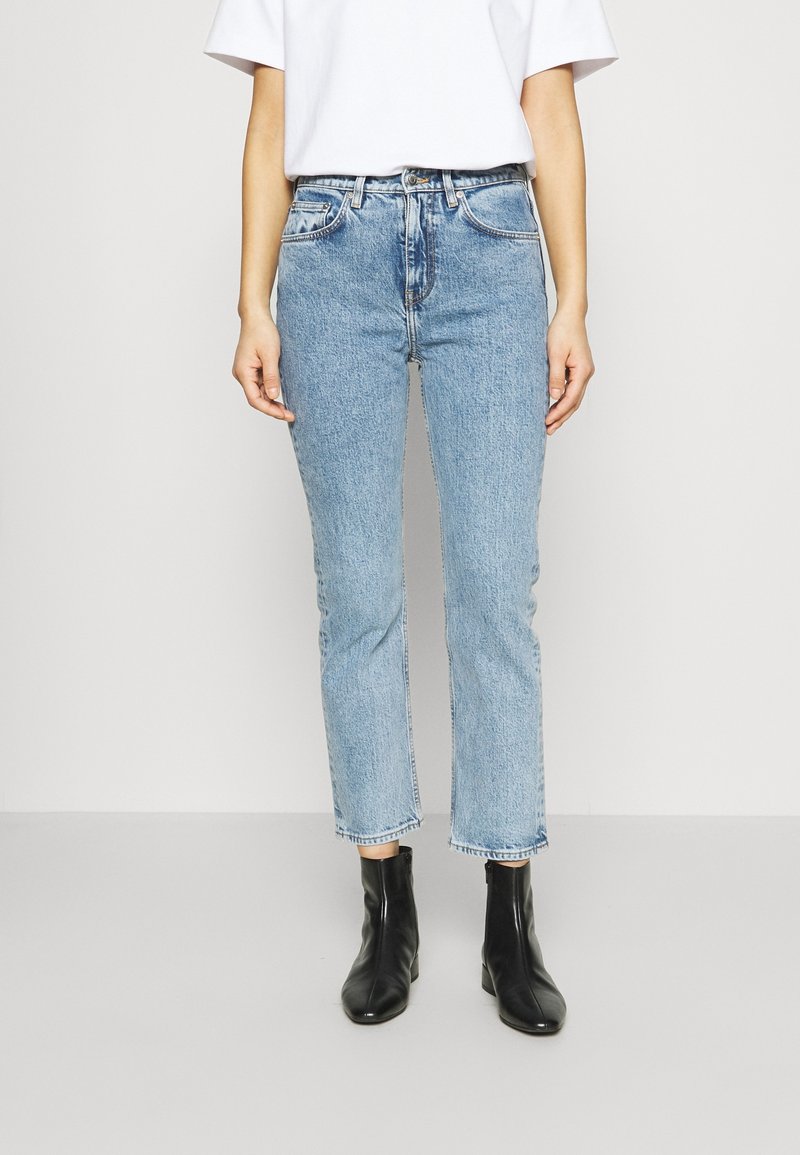 Jeans bleu clair, taille haute, jambes droites, ourlet brut et conception à cinq poches. Associés à des bottines noires.