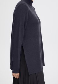 Pull à col roulé en tricot bleu marine foncé avec des poignets côtelés, des fentes sur les côtés et une coupe décontractée, confectionné à partir d'un tissu texturé doux.