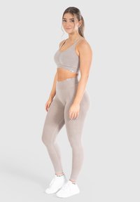 Sujetador deportivo beige claro y leggings de cintura alta fabricados con una tela elástica y texturizada. Presentan un sutil canalé y un acento de logo en ambas prendas.