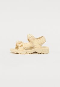 Sandales beiges avec des sangles ajustables, en tissu texturé et semelles rembourrées. Présente un accent floral sur l'avant du pied et une semelle extérieure en caoutchouc durable.