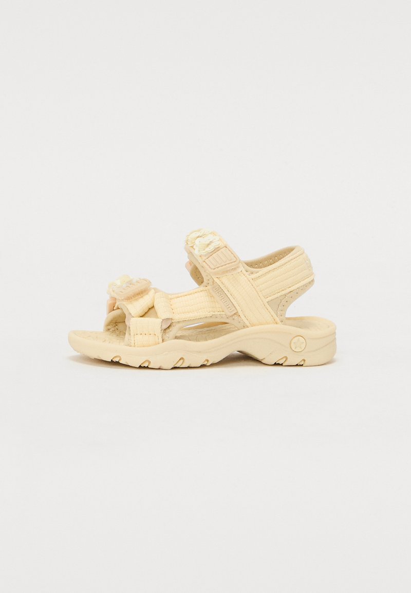 Sandales beiges avec des sangles ajustables, en tissu texturé et semelles rembourrées. Présente un accent floral sur l'avant du pied et une semelle extérieure en caoutchouc durable.