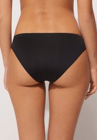 Czarny dół bikini, wykonany z gładkiego materiału. Posiada niski krój i minimalistyczny design, odpowiedni do strojów kąpielowych. Brak wzorów i akcentów.