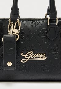 Μαύρη τσάντα με υφή και ανάγλυφο μοτίβο λογότυπου, εξοπλισμένη με εξαρτ ήματα σε χρυσό τόνο. Διαθέτει διπλά χερούλια και ένα εμφανές σημείο με το λογότυπο Guess.