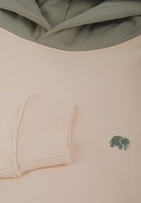 Sudadera rosa claro con capucha verde y puños acanalados, que presenta un pequeño logo de elefante verde en el pecho. Textura suave, diseño casual.