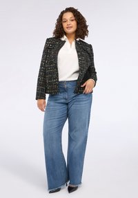 Blazer in tweed nero con paillettes colorate, polo bianca, jeans ampi blu con orli strappati e décolleté nere a punta.