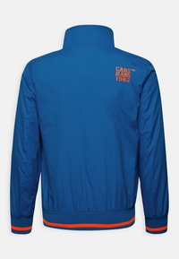 Modrá větrovka s vysokým límcem, žebrovanými manžetami a lemem. Na zadní straně je oranžový nápis "CARS JEANS 1962". Hladká textura.